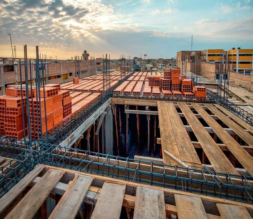 Bird's-eye view of an industrial construction site with stacks of red bricks and wooden planks under a blue sky at sunrise.